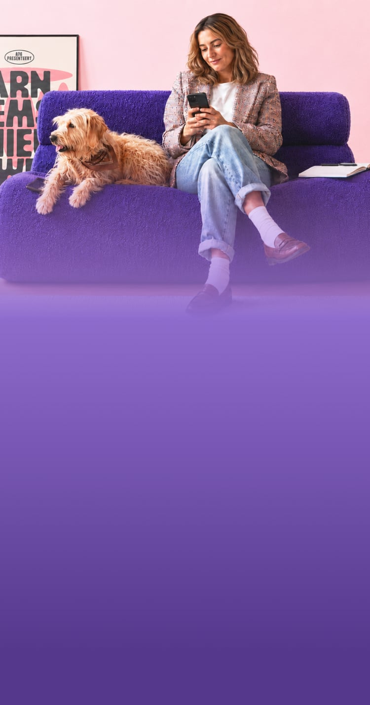 Woman reviewing her phone on a couch with a dog beside her